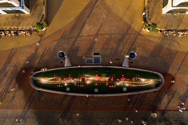 A bird's-eye view of a GTA 6 player strategically positioned on a rooftop overlooking a group of enemies near a stack of explosive barrels. The player is aiming their weapon, ready to detonate the barrels.